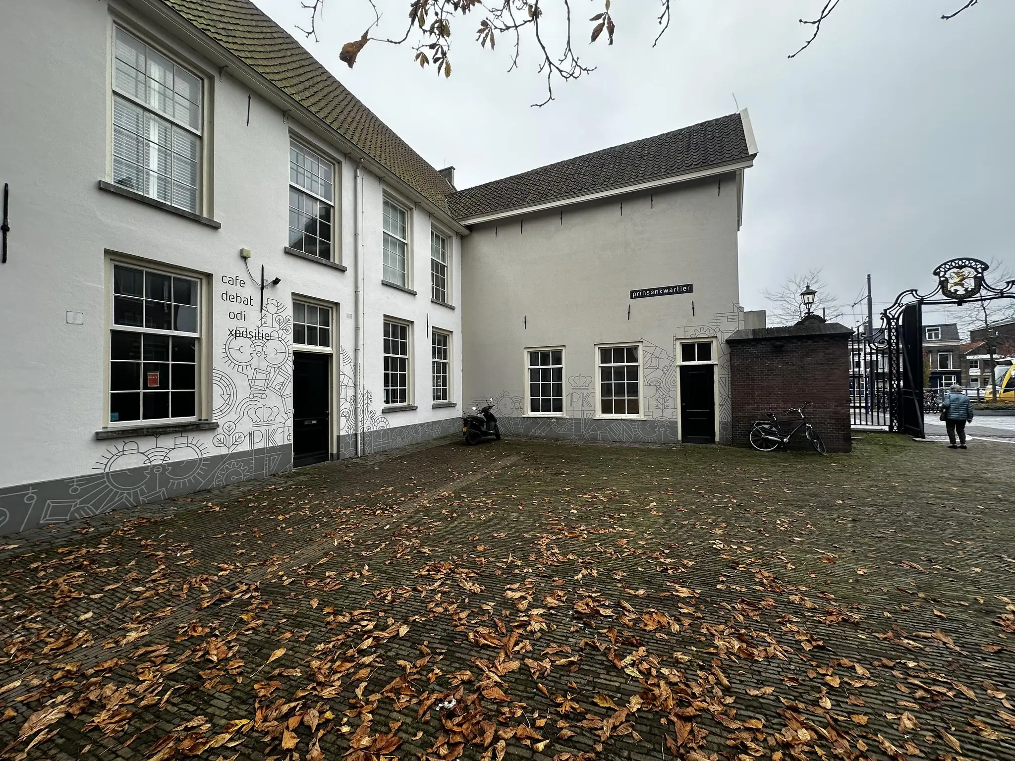 Wit gebouw aan het Sint Agathaplein met opschrift "Prinsenkwartier" en herfstbladeren op de grond.